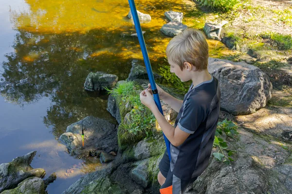 少年は フックと餌を準備して 釣り棒をキャストする準備をします 夏の川でのスポーツ釣り — ストック写真