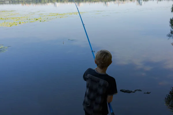 ティーンエイジャーは棒の背中に立って ニブルを待ちます 夏の川でのスポーツ釣り — ストック写真