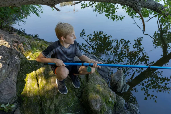 岩の上に座って魚を捕まえる少年 夏の川でのスポーツ釣り — ストック写真