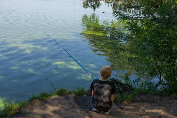 A teenager with his back turned is fishing with a cast rod. Sport fishing on the river in summer.