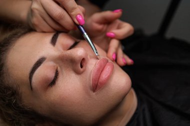 Usta, kalıcı makyajdan önce dudaklarının etrafına boyama kremi sürüyor. Sarışınlar için hassas daimi dudak makyajı