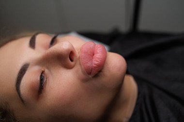 Kız model kalıcı makyajdan önce dudaklarını öpücüğe çeviriyor. Sarışınlar için hassas daimi dudak makyajı