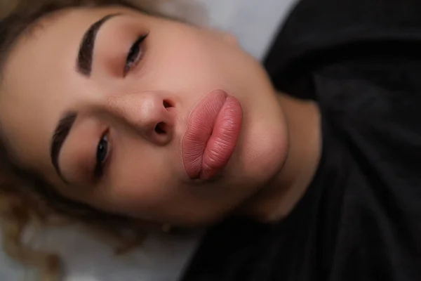 Girl model twists her lips into a kiss before permanent makeup. Delicate permanent lip makeup for blondes