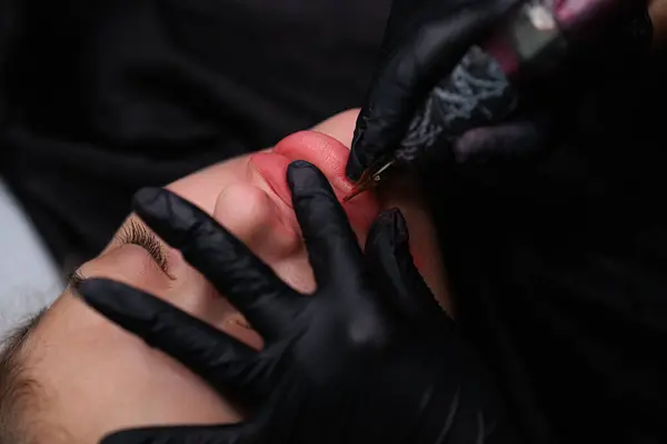 Permanent lip makeup second pass over the lips with a tattoo machine. Delicate permanent lip makeup for blondes