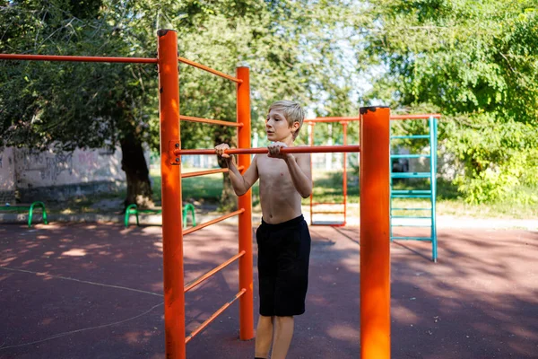 Sports boy performs exercises on the horizontal bar. Street workout on a horizontal bar in the school park.