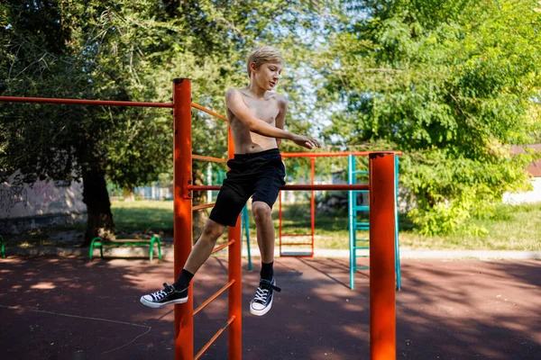 The teenager plays sports. Street workout on a horizontal bar in the school park.