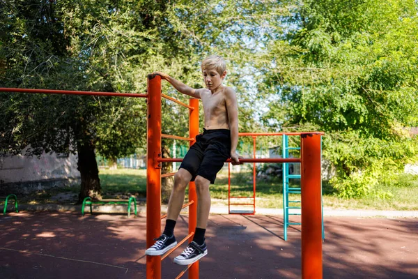 The teenager goes in for sports. Street workout on a horizontal bar in the school park.