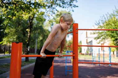 Atletik çocuk kendini uzattı ve elleriyle yatay çubuğa tutundu. Okul parkındaki yatay bir barda sokak çalışması..