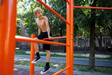 Gençler spor barlarının arasına tırmandı. Okul parkındaki yatay bir barda sokak çalışması..