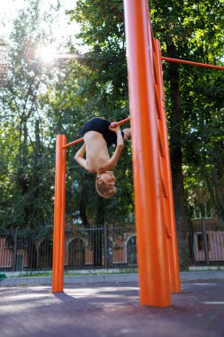 Parktaki bir genç, kafasıyla barın dibindeki bara asılarak spor yapmaya gider. Okul parkındaki yatay bir barda sokak çalışması..