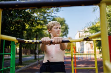 Çocuk atletik koşumların korkuluklarına tutunuyor. Okul parkındaki yatay bir barda sokak çalışması..