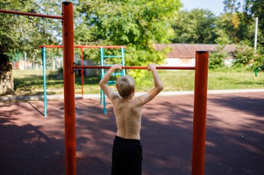 Genç, spor barına tutunarak ayakta duruyor. Okul parkındaki yatay bir barda sokak çalışması..