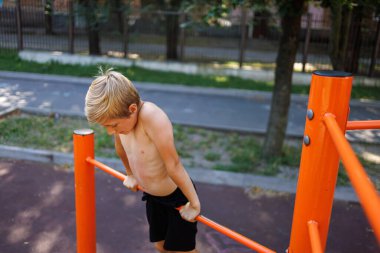  Atletik bir genç ağırlığını yatay bir çubukta taşır. Okul parkındaki yatay bir barda sokak çalışması..