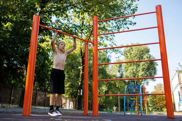 The teenager grabbed the horizontal bar with his hands and tried to climb up. Street workout on a horizontal bar in the school park.
