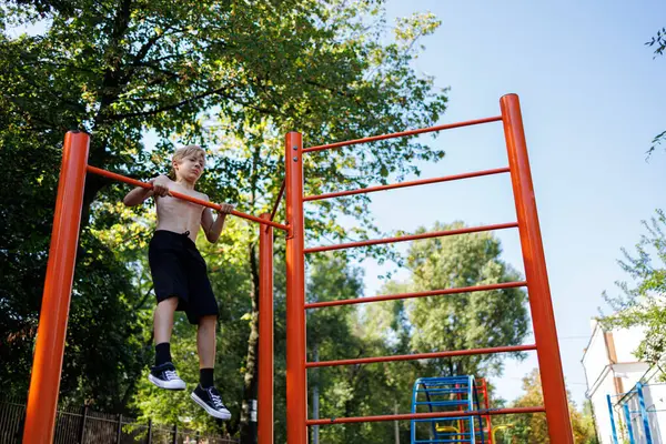 Sports boy performs pull-ups on the horizontal bar. Street workout on a horizontal bar in the school park.