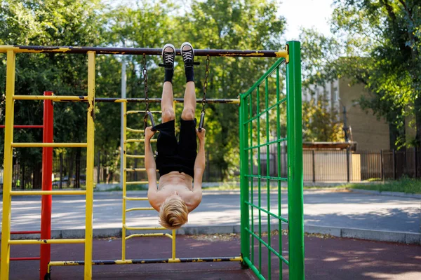 Çocuk spor yüzüklerini baş aşağı asmış, elleriyle tutuyormuş. Okul parkındaki yatay bir barda sokak çalışması..