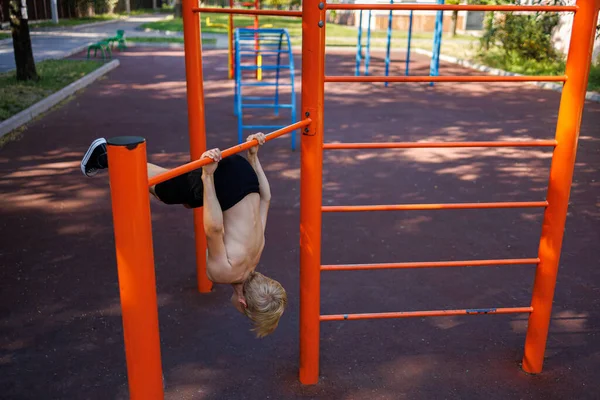 an athletic child caught his hands on the horizontal bar and bent back. Street workout on a horizontal bar in the school park.