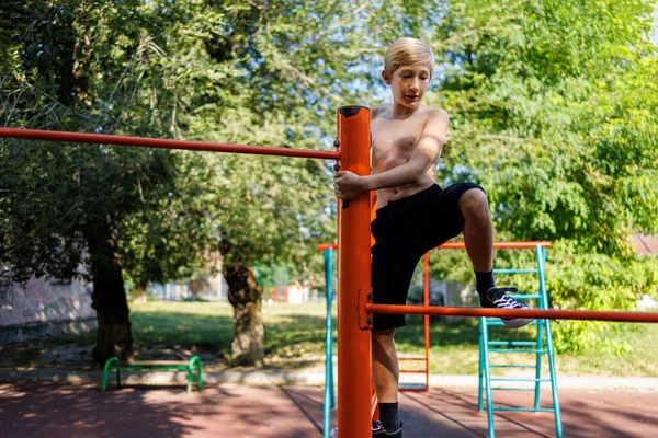 The boy in the school park climbed to the top of the horizontal bar. Street workout on a horizontal bar in the school park.