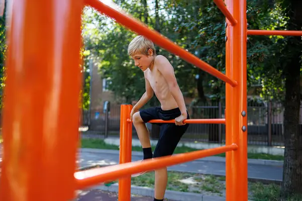 A fitness child climbed between the sports bars. Street workout on a horizontal bar in the school park.