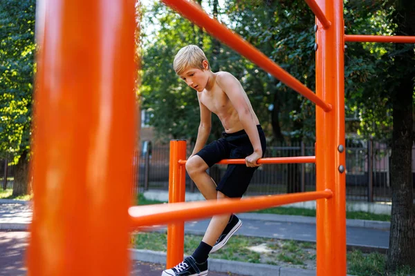 A fitness kid climbed between the gym bars. Street workout on a horizontal bar in the school park.