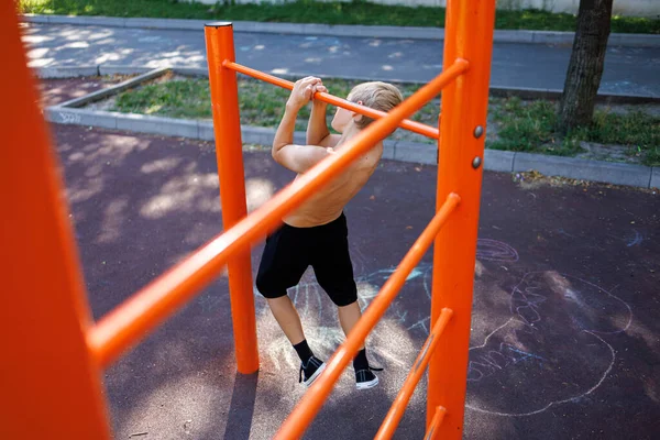 A teenager pulls up on the crossbar between sports horizontal bars Street workout on a horizontal bar in the school park.