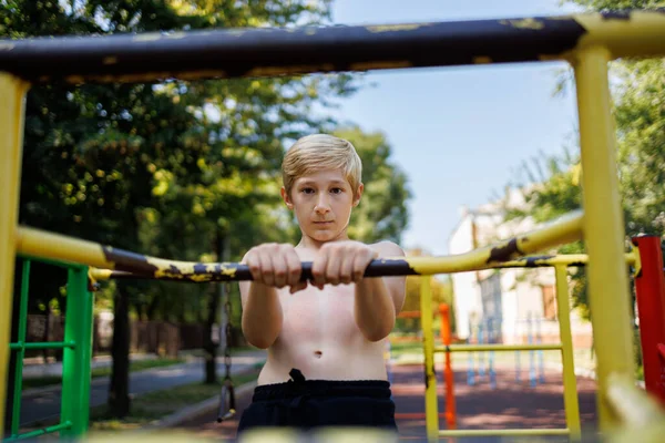 The child holds on to the handrails of the sports horizontal bars. Street workout on a horizontal bar in the school park.