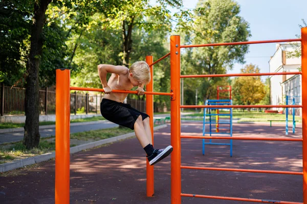 The boy is trying to climb the sports bar. Street workout on a horizontal bar in the school park.