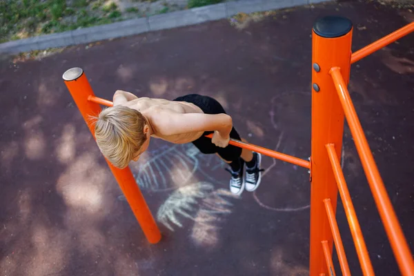 A teenager stretched out holding onto his arms and performing acrobatic exercises on a horizontal bar. Street workout on a horizontal bar in the school park.