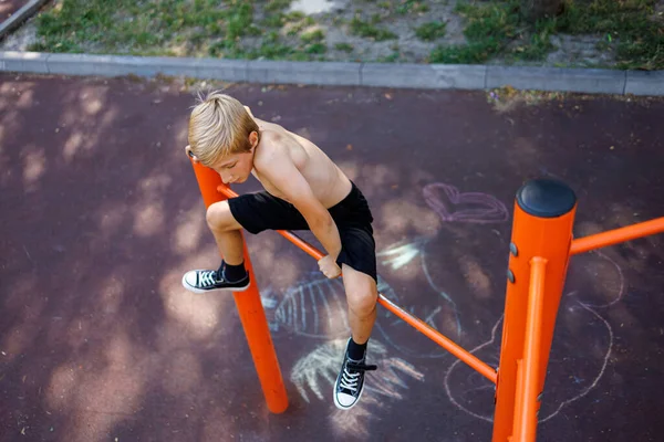A sports boy climbed up the horizontal bar to perform a sports element. Street workout on a horizontal bar in the school park.