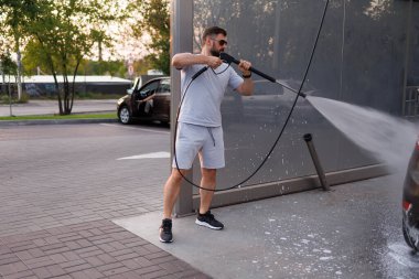 Bir adam arabaları yıkamak için bir su topu tutar. Bir araba yıkama servisinde bir araba..