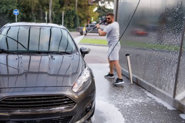Arabanın önünü yıkamak arka plandaki adam tarafından yıkanmak. Otomobil yıkamada bir araba..