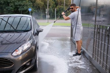 Bir adam arabanın kirini bir su topuyla iyice yıkar. Otomobil yıkamada bir araba..