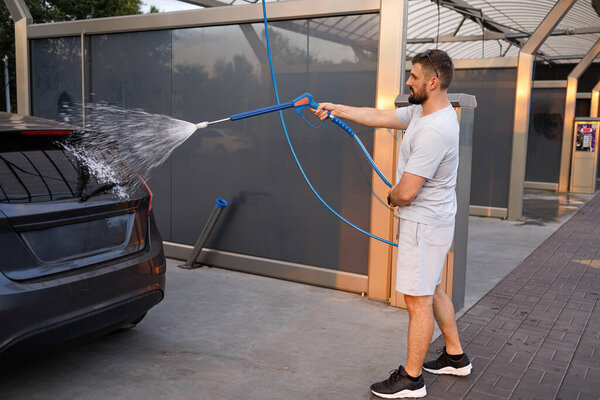 A man points a foam sprayer at a car. A car at a self service car wash.
