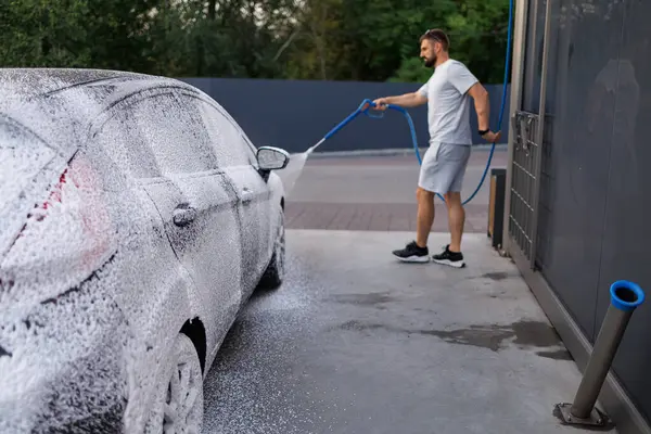 The side of the car is covered with foam, the person in the background is applying foam to the car. A car at a self service car wash.