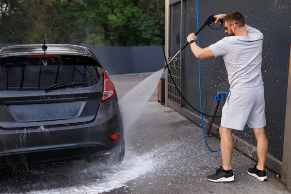The car\'s at a car wash run by a man with a water cannon. A car at a self service car wash.