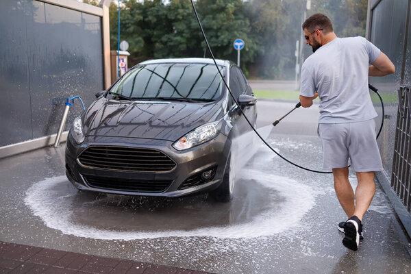 At a car wash, a man washes his car. A car at a self service car wash.