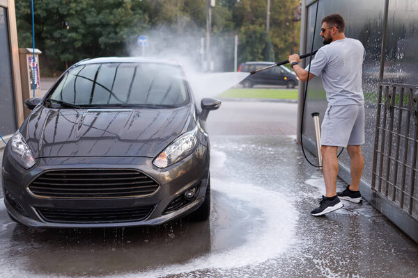 At a car wash, a man washes his car. A car at a self service car wash.