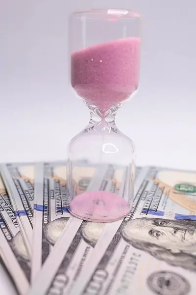 There is an hourglass transparent on the money bills. The hourglass is located near the dollar bills.