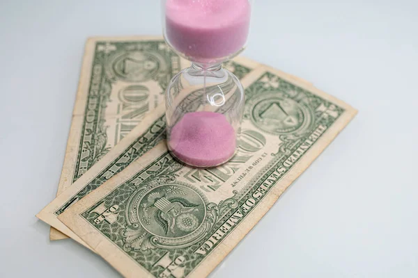 One dollar bills have hourglasses on them. The hourglass is located near the dollar bills.