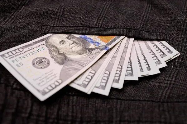 A pile of $100 bills peeks out of his pocket. Dollar bills sticking out of your pocket.