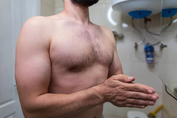The body of a man standing in the bathroom. A man with an athletic figure in the bathroom.