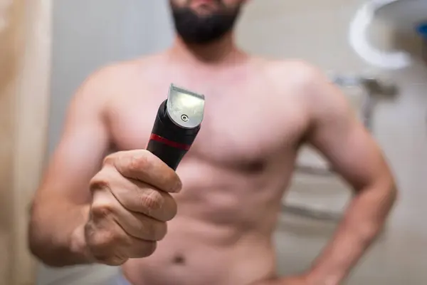 男は目の前に電気シェービング装置を持っている バスルームにスポーツフィギュアを持つ男 — ストック写真