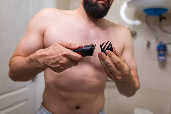 A man demonstrates the electric razor he holds in his hand. A man with an athletic figure in the bathroom.
