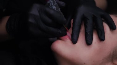 Model dudakların yakın plan, parmakları usta tarafından tutulan ve değişikliklerin dudaklarında yapılan dövme makinesi kalıcı makyaj prosedürü yardımıyla 