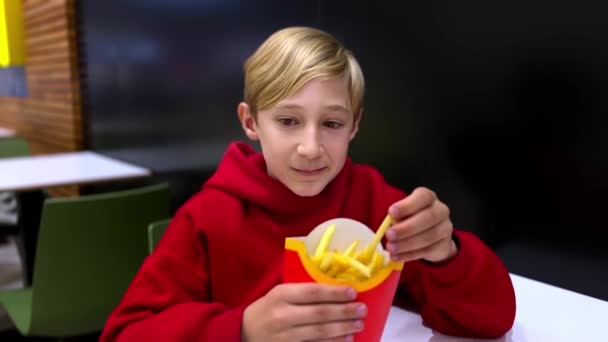 男の子は深いフライヤーから揚げ物を食べるテーブルに座っている ファーストフードを食べるレストランの男の子 — ストック動画