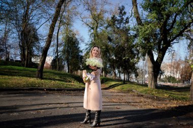 Sonbaharda bir sonbahar parkında ceketli bir iş kadını elinde bir buket beyaz gülle ceketli şık bir kadın..