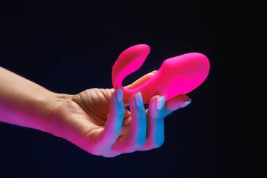 Küçük boy vibratör, kızın elinde kırmızı renkli oyunlar için. Siyah arka planda neon ışıkları olan bir seks oyuncağı klitoral vibratörü..
