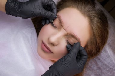 Kalıcı makyaj işleminden önce, usta modelin kaşlarındaki bir iplikle işaret koyuyor. PMU Prosedürü, Kalıcı Kaş Makyajı.