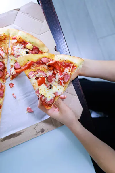 The child's hands take a piece of pizza out of the box  Sausage and cheese pizza.