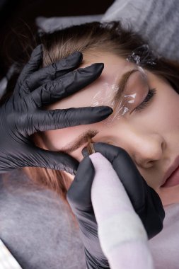 Kalıcı makyaj kartuşuna sahip bir dövme makinesi kaş derisine pigmentler yerleştirir. PMU Prosedürü, Kalıcı Kaş Makyajı.